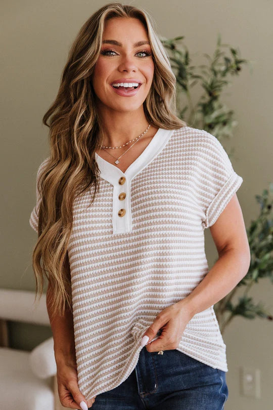 Woman wearing a beige short-sleeve shirt with buttons, standing indoors.